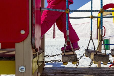 winter, cold, snow. A girl in a pink suit climbs the stairs. They are made of wood and swing. almost...