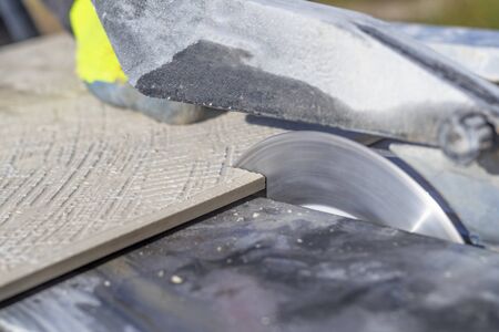 outdoors. sunny day. a man in yellow gloves saws a tile for the floor. machine with special circles.の写真素材