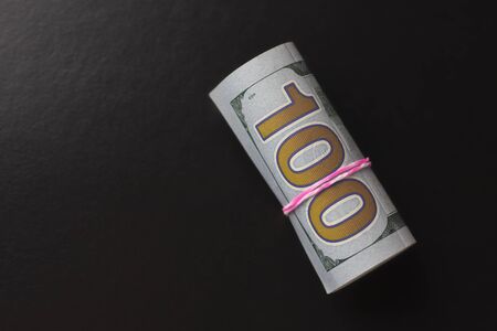 Black background. close-up. 100 dollars you rolled up and tied an elastic band.の写真素材