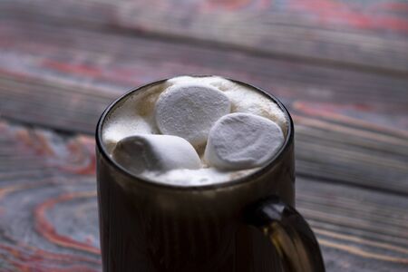 Marshmallow. Retro style wooden background. Glass mug with marshmallow in it. There is also a woolen...