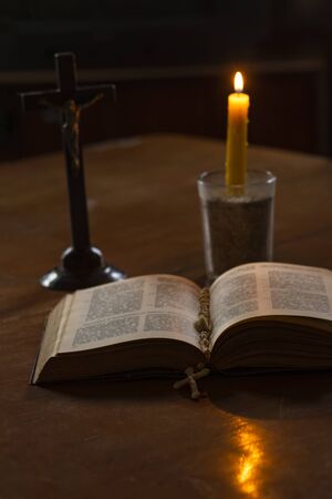 Wooden stained glass table. There is a book on it. on it is a cross, a candle is burning. Dim...