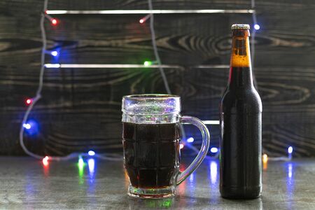 wooden background, mug and bottle of dark beer with foam. Copy space. Close-up