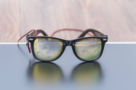Sunglasses are on the monitor. The sky is reflected in them. Tinted.