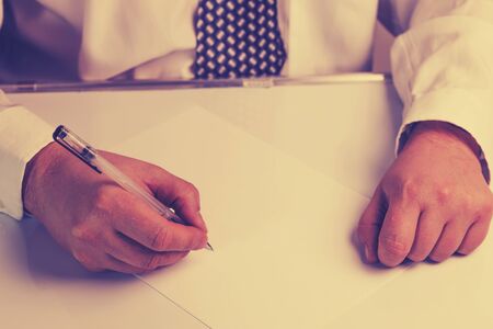 businessman writes on a sheet of white paper. Dressed in a shirt and tie. Close-up. There is a tint.の写真素材