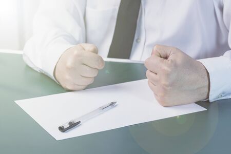 businessman clenched his fists next to a white sheet of paper. Wood background. Dressed in a shirt and tie. Close-up.の写真素材