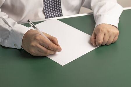 businessman writes on a sheet of white paper. Wood background. Dressed in a shirt and tie. Close-up.