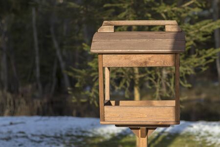 A wooden bird feeder in a dark forest stands on the ground. Shallow depth of field. There is a tint.の写真素材