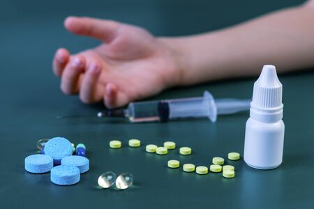 child's hand in the background no focus. In the foreground are pills. And an injection syringe. Close-up.の写真素材
