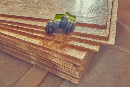OSB slab building material made from reborn sawdust. They lie in a pile, yellow protective gloves lie on it. Close-up.の写真素材