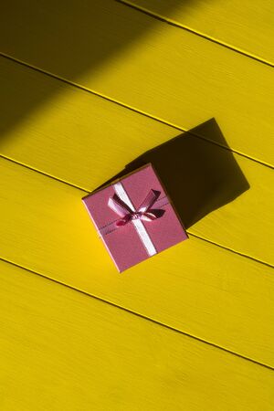 Rough shadow. Retro yellow wooden background. Gift box in pink.の写真素材