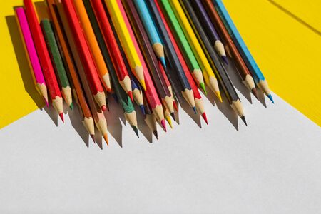 Rough shadow. Bright sunshine. Retro yellow wooden background. In the center, a sheet of paper with drawings and around lined with pencils of different colorsの写真素材