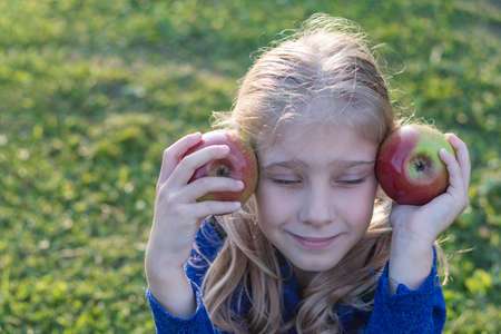 soft focus. Daylight. A girl with white hair holds two red apples in her hands. The sun is low.の写真素材