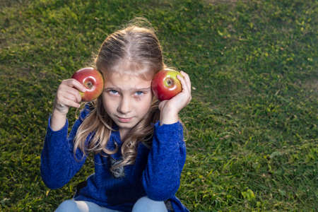 soft focus. Daylight. A girl with white hair holds two red apples in her hands. The sun is lowの写真素材