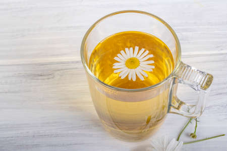 White wooden background in retro style. On it is a glass mug in which chamomile tea is brewed. Copy space. textの写真素材