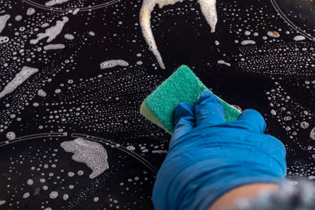 girl in blue household gloves washes the electric stove. Applies a special solution. Close-up