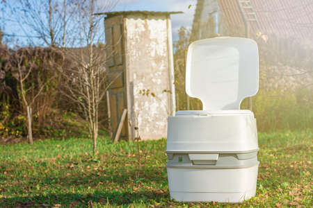 Street lighting. a portable plastic toilet in the foreground. In the background is a wooden street lavatory with a broken doorの写真素材