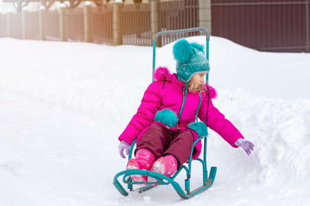 Street lighting. winter is a lot of snow. a beautiful girl in a red jacket and a green hat is sleddingの写真素材