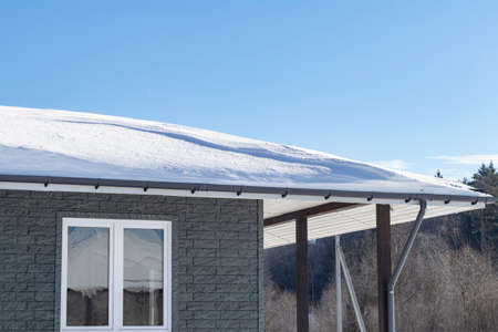 Snow drift on roof after of snowfalls on sunny day. Wooden house in the snow.