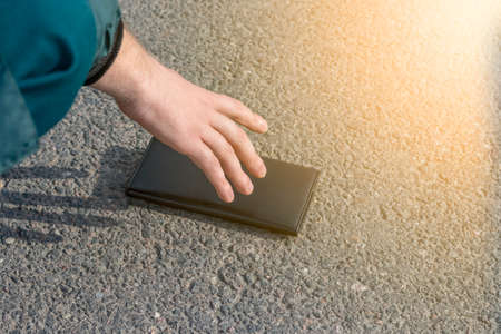 Street lighting. there is a wallet on the road on a sunny summer day. A human hand reaches out to...