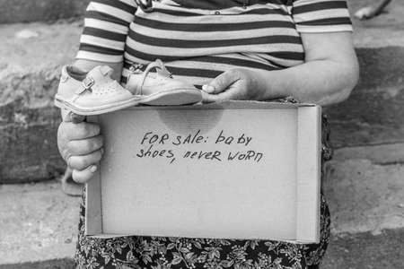 Black and white photo. A woman with elderly hands holds sandals. The inscription about the sale