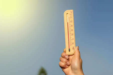 Natural lighting. a human hand holds a wooden thermometer. The temperature on it is very high. Heat