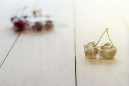 White wooden background in retro style. Red cherries in ice cubes. Close-up
