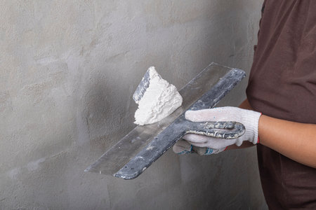Studio lighting. the master on a metal spatula applies the solution to the wall for leveling. Close-up.の写真素材