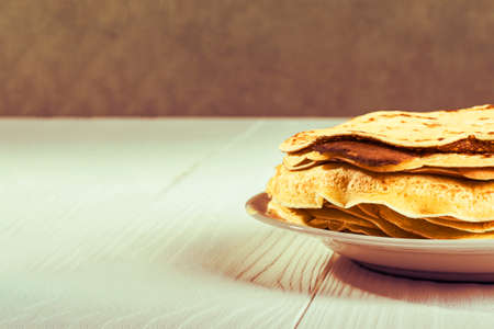 white wooden background in retro style. the plate in it is thin yellow pancakes. close-up