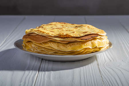 white wooden background in retro style. the plate in it is thin yellow pancakes. close-up