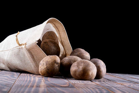 studio lighting. black background. potatoes are planted from a bag on a retro-style wooden background. close-up.の写真素材