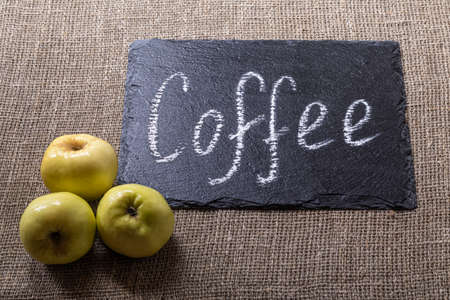 coffee. an inscription on a black stone in white chalk. taken on a burlap bag next to three yellow applesの写真素材