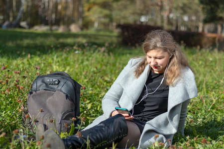 Portrait of a young beautiful Caucasian happy woman, about 35 years old with long hair and headphones in her ears. Cute girl walking in the park, close-upの写真素材