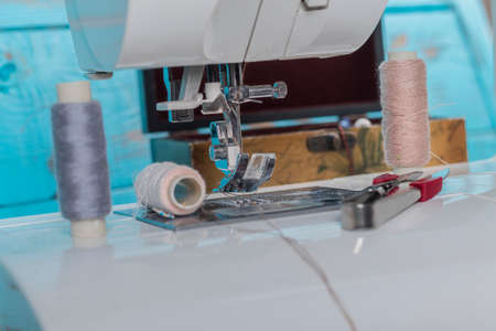 sewing machine. a foot and a needle with a thread in the center of attention. close up. there is a...
