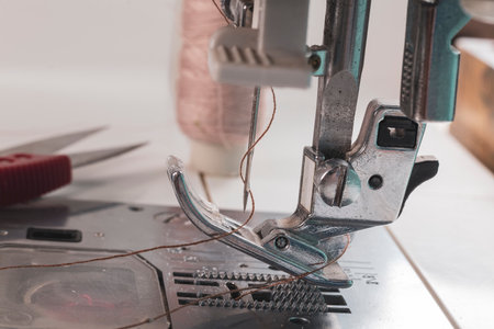 sewing machine. a foot and a needle with a thread in the center of attention. close up. there is a...