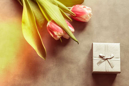 wooden background. there are tulips on it, several pieces. golden gift box.