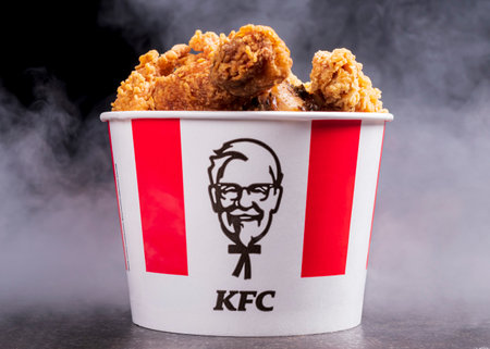 Minsk, Belarus - December 03, 2021: black background, night. Lots of hot wings or strips of KFC chicken in a KFC Kentucky Fried Chicken fast food bucketのeditorial素材