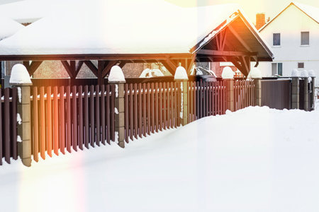 natural light. winter. a lot of snowdrifts. brown metal picket fence. around a wooden house. installation and saleの写真素材