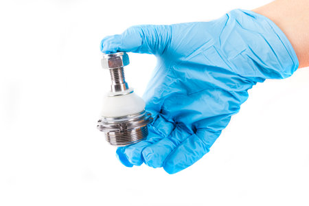 a metal part of the car suspension. A human hand in blue gloves holds the hinge that turns the...
