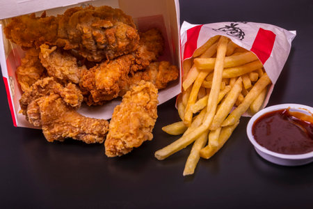 Minsk, Belarus June 19, 2024: black background, night. Lots of hot wings or strips of KFC chicken in a KFC Kentucky Fried Chicken fast food bucketのeditorial素材
