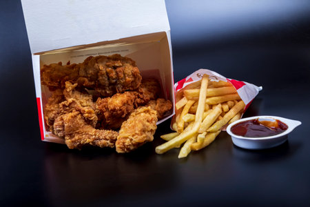 Minsk, Belarus June 19, 2024: black background, night. Lots of hot wings or strips of KFC chicken in a KFC Kentucky Fried Chicken fast food bucket.のeditorial素材