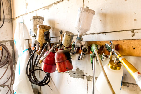 Paint spray gun. Wall in the workshop, on the wall hangs a number of painting equipment. Coat for...