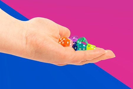 A hand displays a vibrant variety of plastic dice in multiple colors.の写真素材