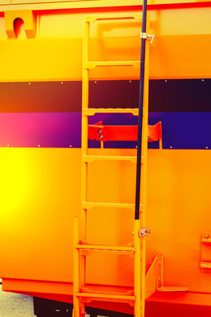 Colorful industrial ladder attached to a bright orange cargo container showcased during daylightの写真素材