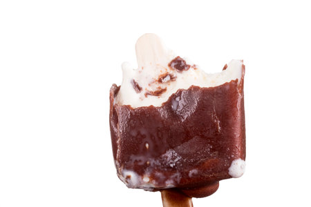 A chocolate ice cream pop is held up on a wooden stick, showing its smooth texture and creamy...