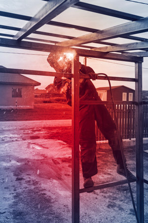 A skilled metalworker engages in welding a metal frame in a residential area, surrounded by trees...