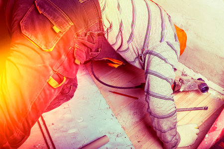 A person in gloves is using a pipe cutter on a wooden floor during a home improvement task. The setting indicates a DIY project, showcasing active craftsmanship.の写真素材