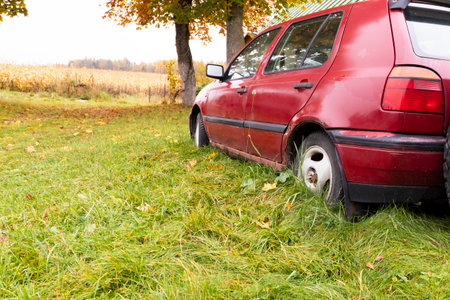 Old abandoned car resting in a field surrounded by trees during the autumn season in a rural areaの写真素材
