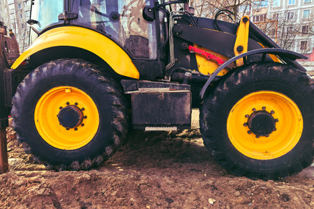 Yellow tractor wheels parked on soil heavy tread caked with mud, sun faded paint on fender,...