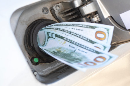 A person is putting cash into a gas pump to pay for fuel. The scene captures the activity of buying...