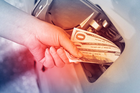 A person is putting cash into a gas pump to pay for fuel. The location shows a gas station with a...